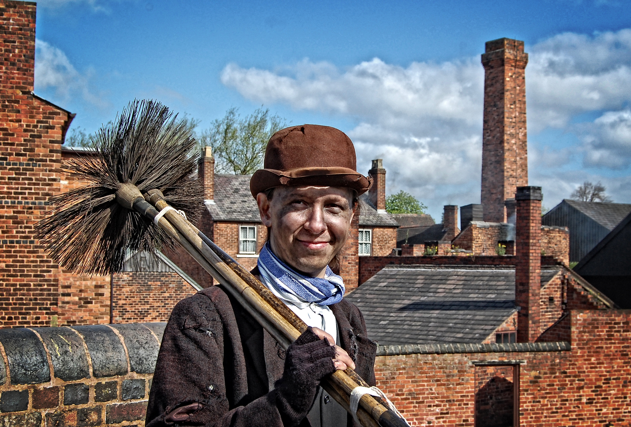 Historic Chimney sweep with a very dirty face and many roofs and chimneys in the background.