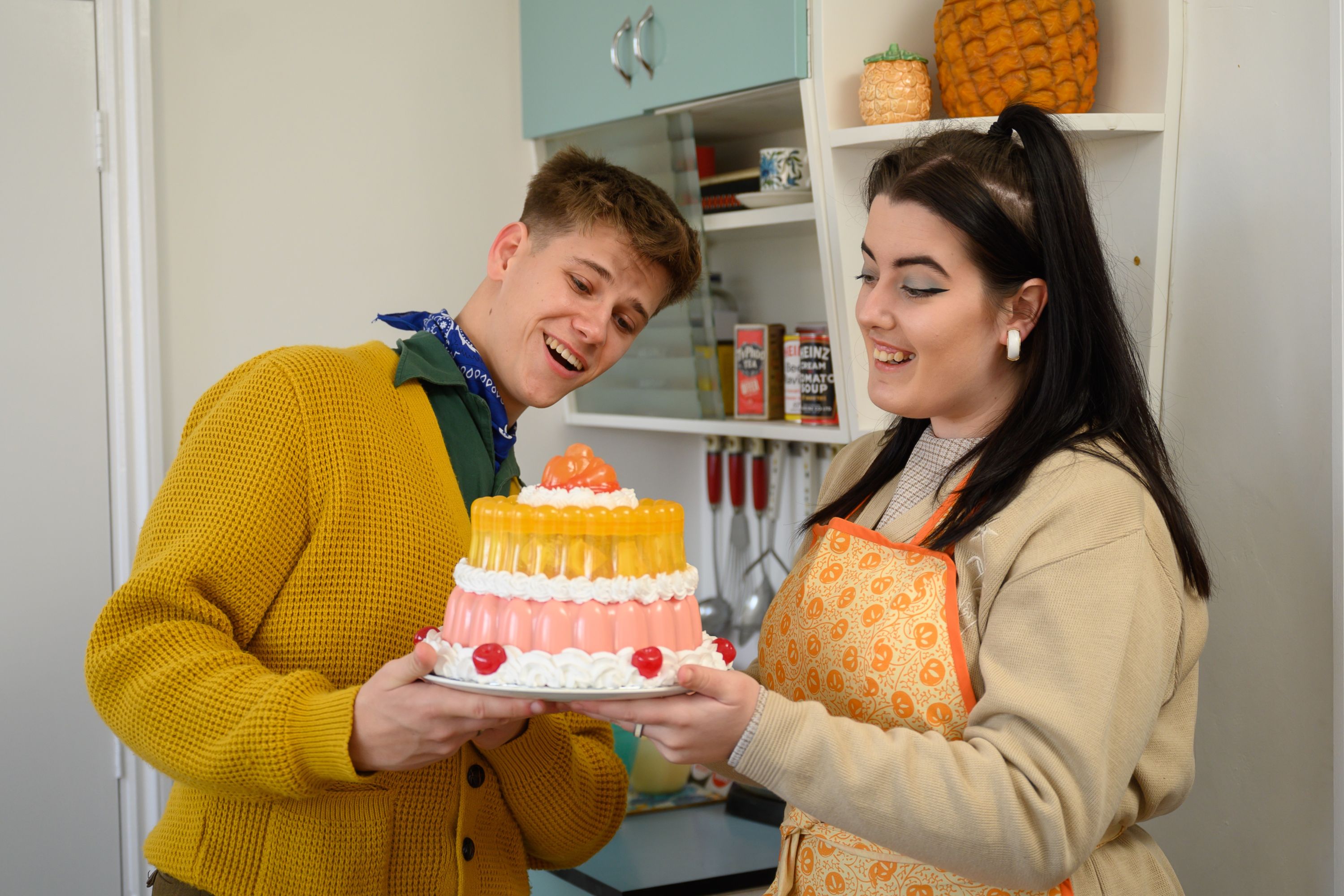 Two historic characters looking at a colourful Blancmange