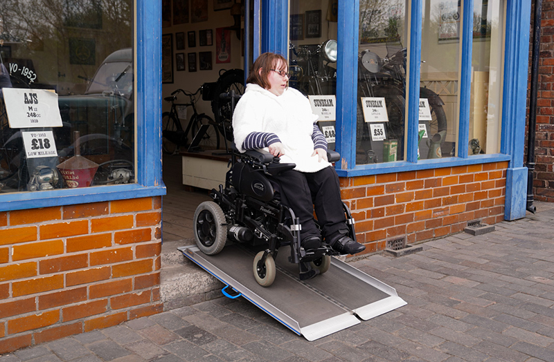 A photograph shows a person in a motorised wheelchair using a ramp to leave a recreated shop.